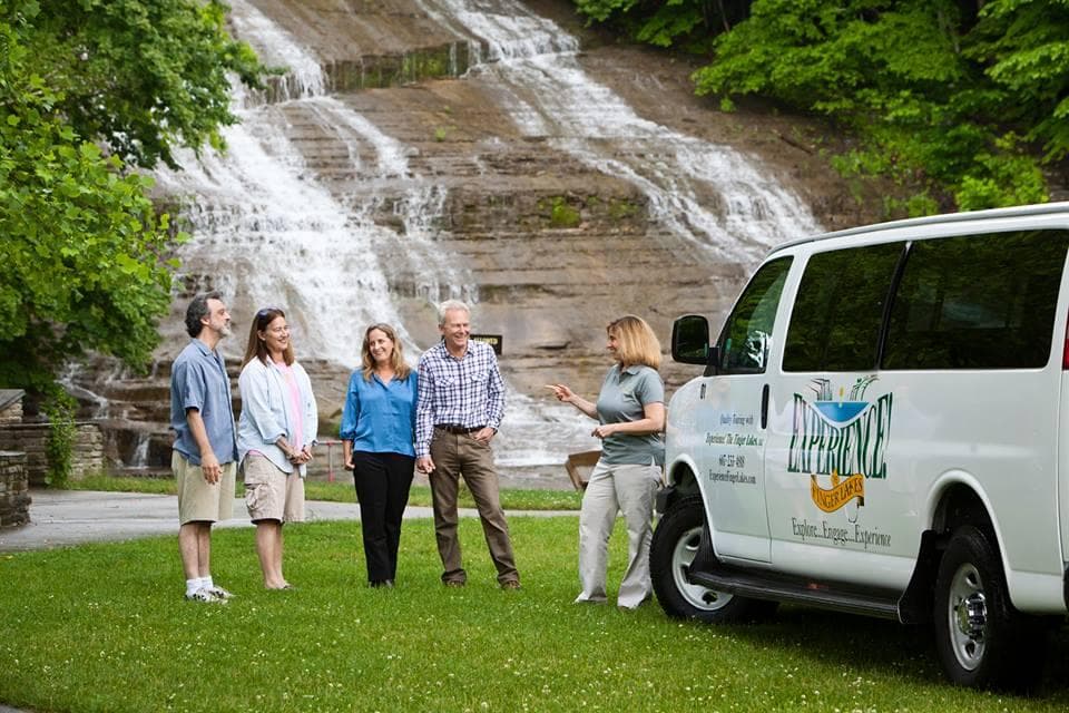 Tour group standing by roadside waterfall with Experience Finger Lakes van