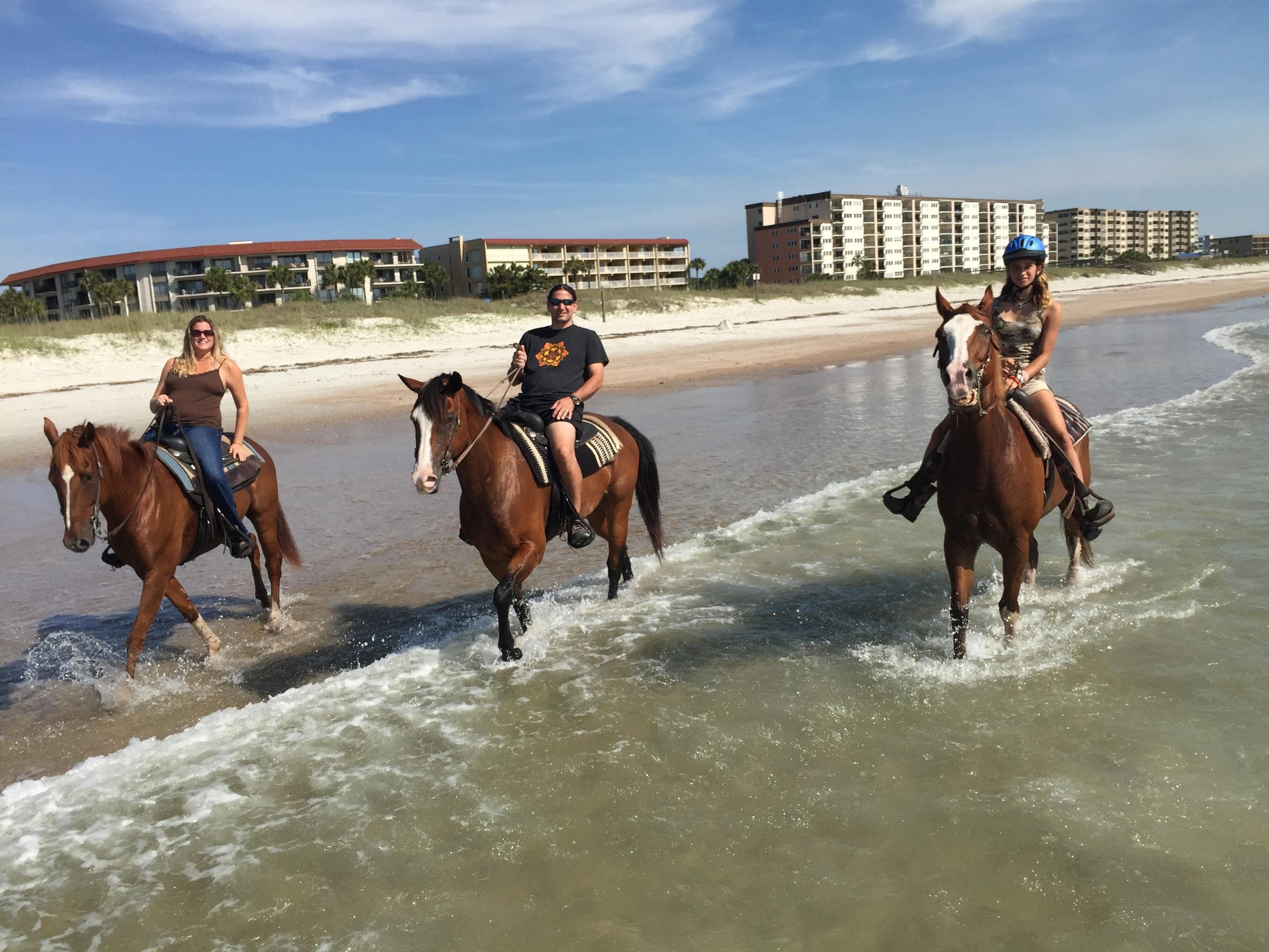 Three riders galloping through surf on sunny coastal beach
