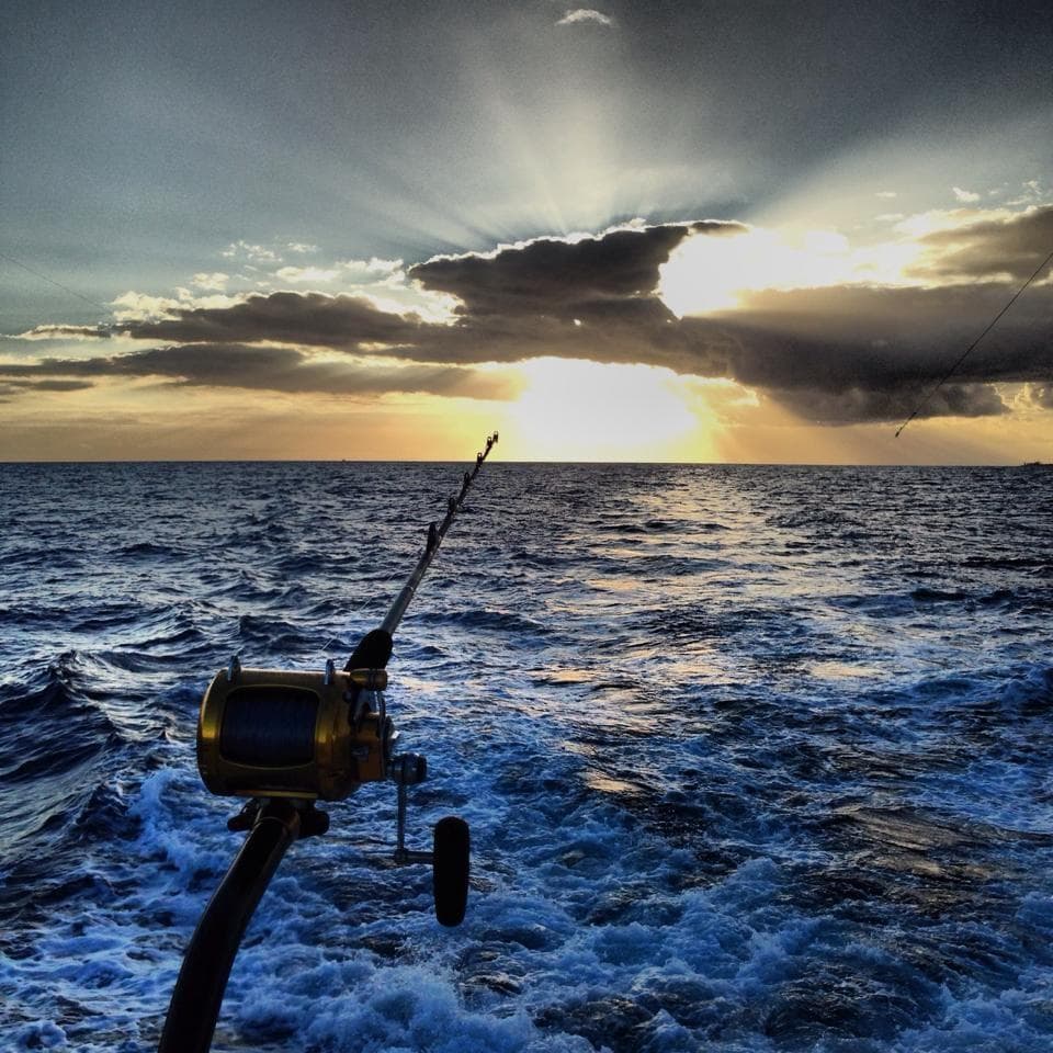 Fishing rod and reel trailing at sunset over open ocean, dramatic sky