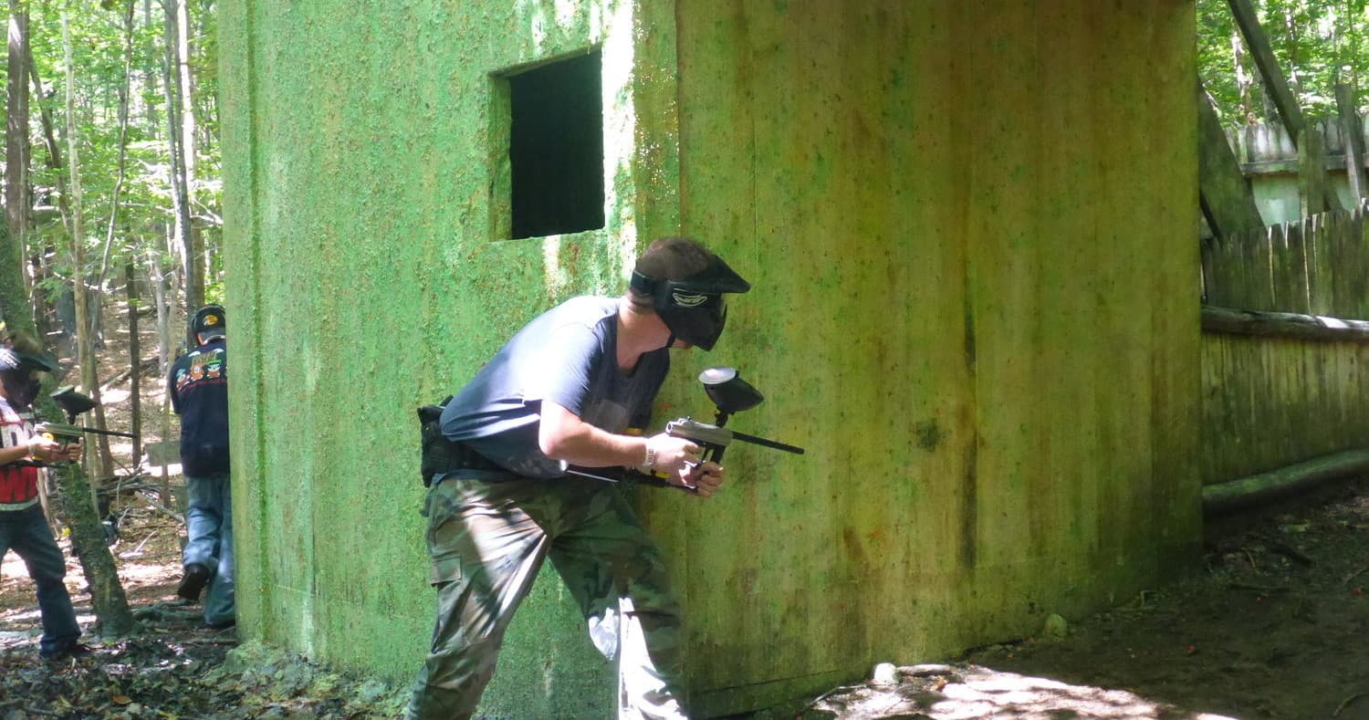 Paintball player firing from bunker in forested outdoor field