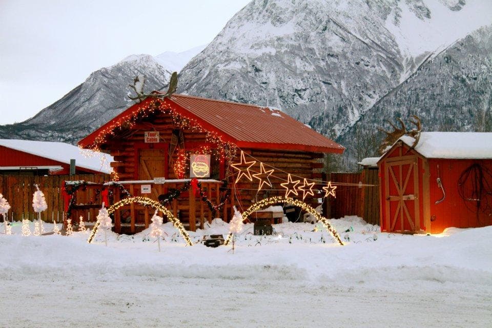 Snowy reindeer farm cabin with mountain peaks and festive decor