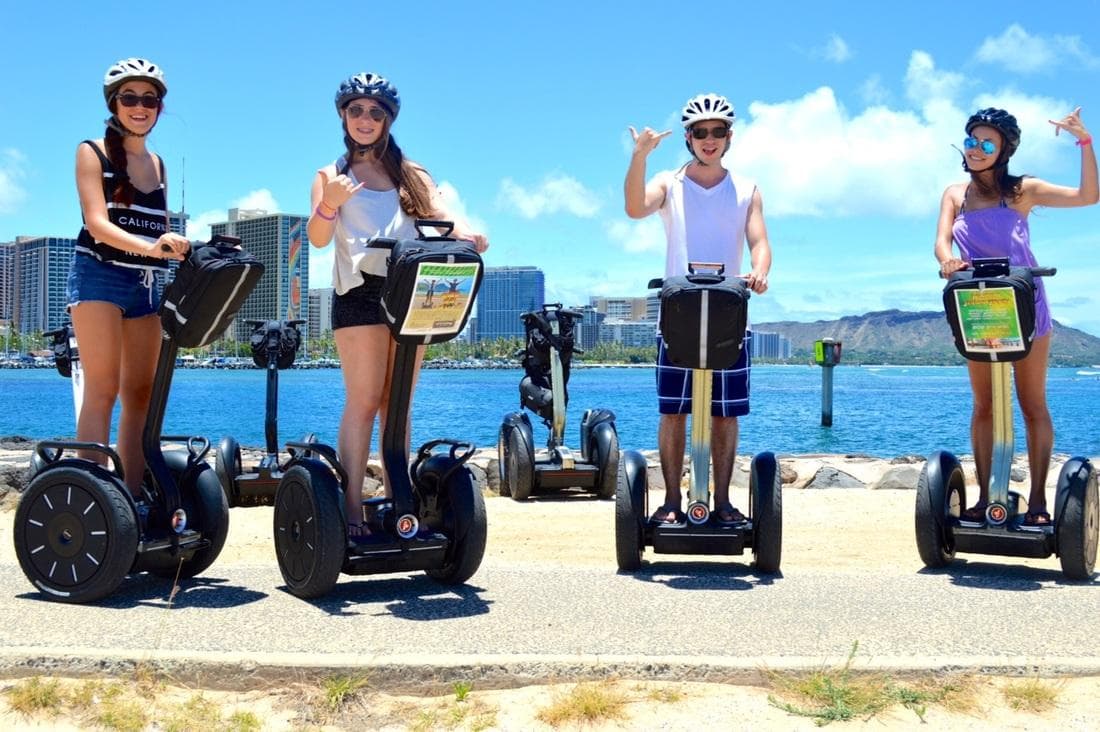 Four riders on Segways by Waikiki waterfront under clear sky