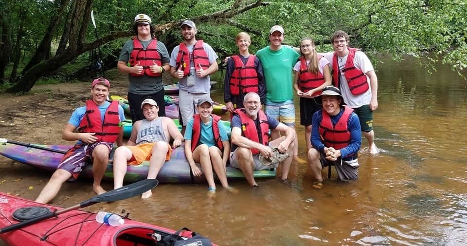 Group of paddlers resting on riverbank with kayaks, outdoor outfit