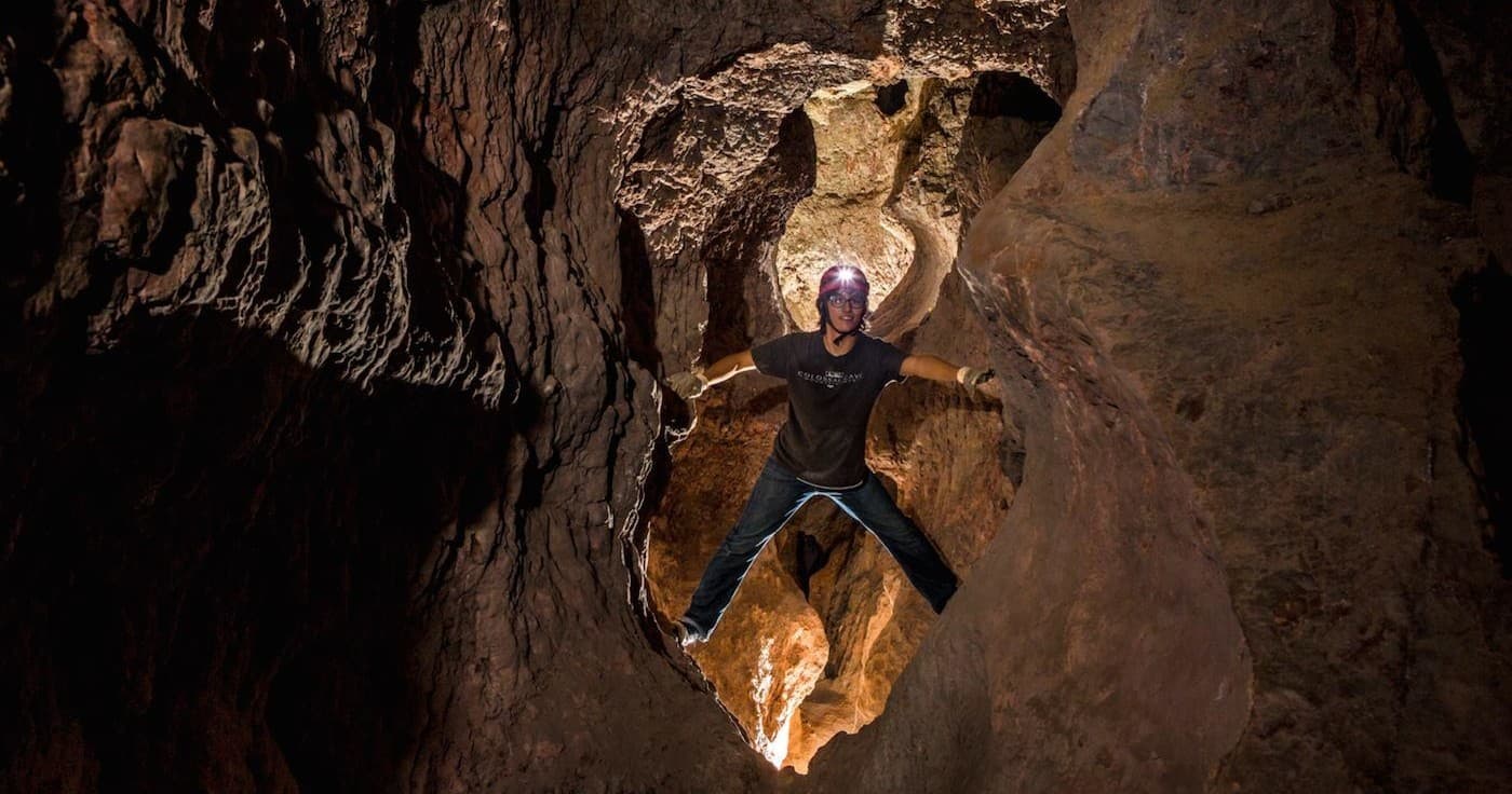 Solo caver traversing narrow cave opening in Colossal Cave, adventurous climb