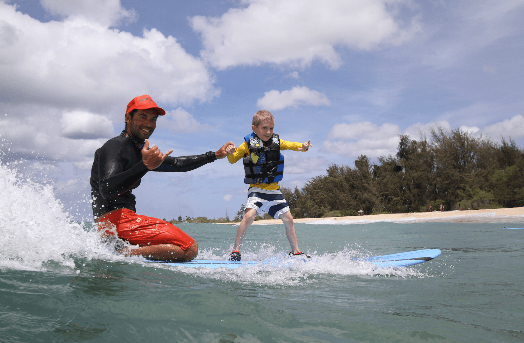 Instructor guiding young child standing on surfboard in shore break