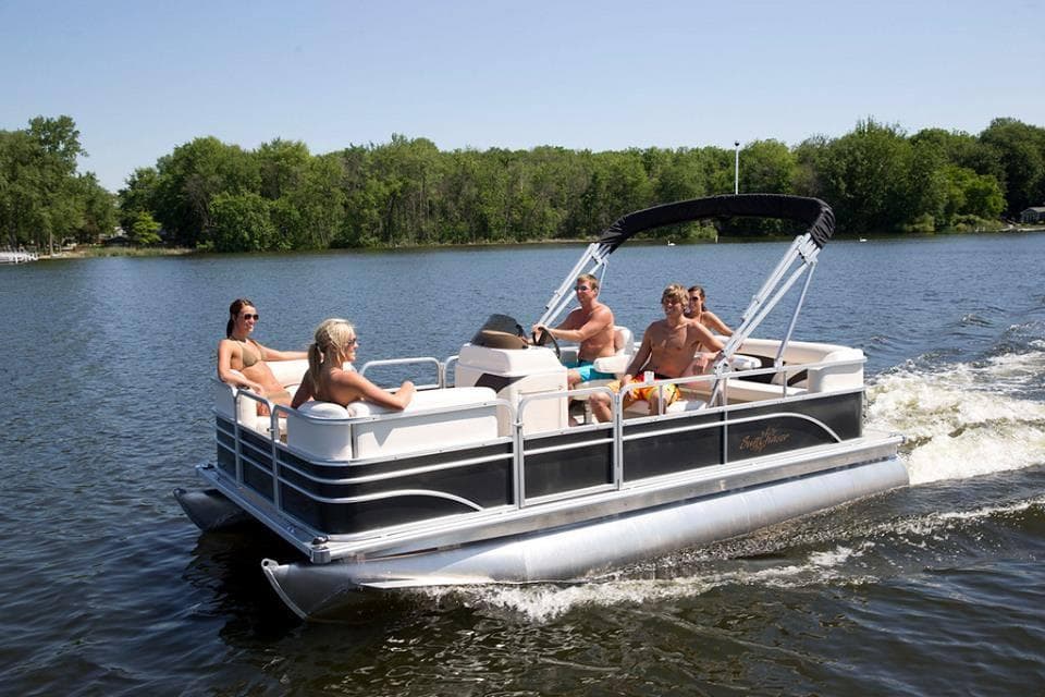 Group cruising on pontoon boat on calm lake with sunlit trees