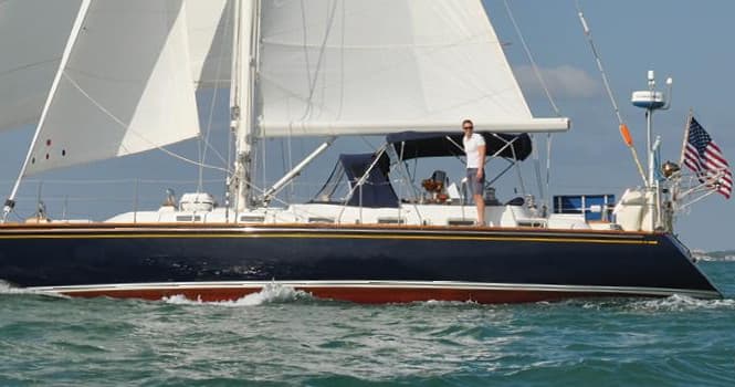 Side view of cruising sailboat on open sea with crew visible