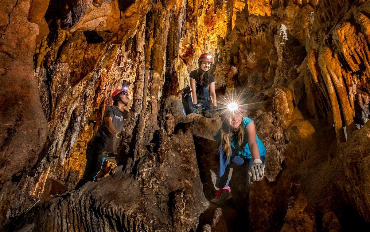 Group cavers exploring illuminated Colossal Cave chamber, climbing rocks