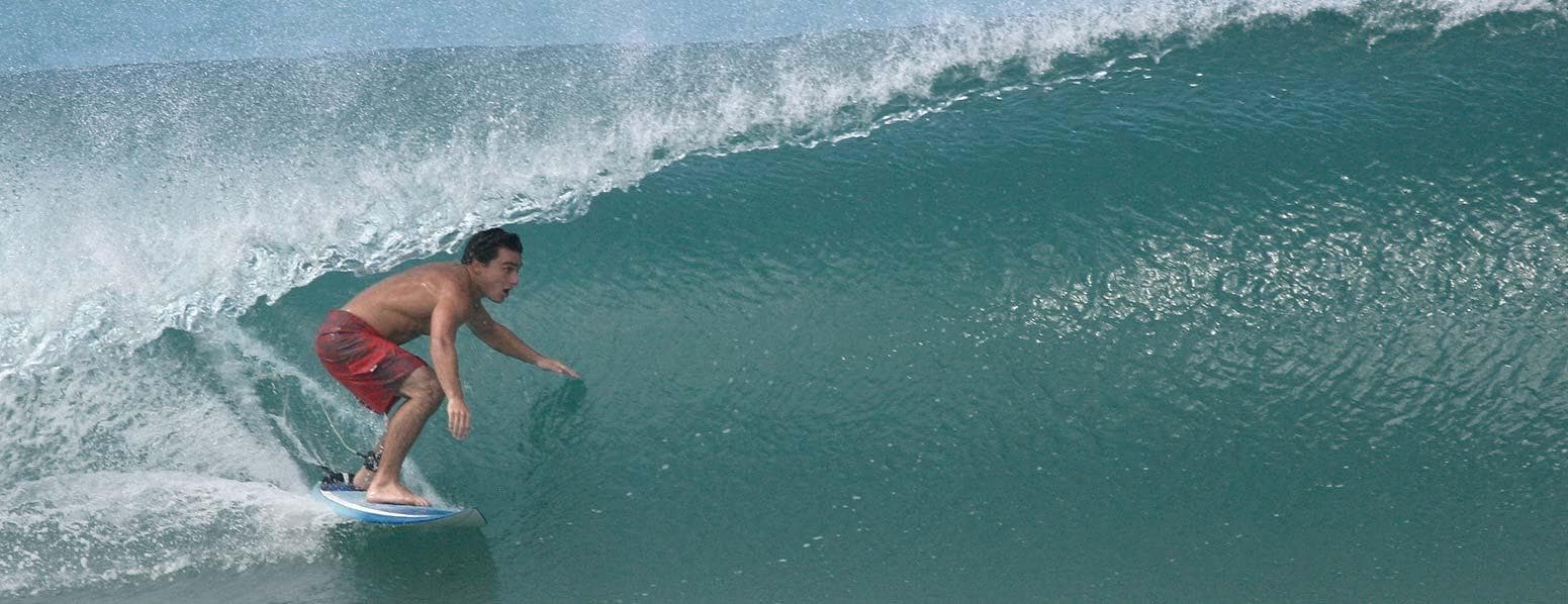 Surfer riding deep ocean barrel wave off tropical coastline