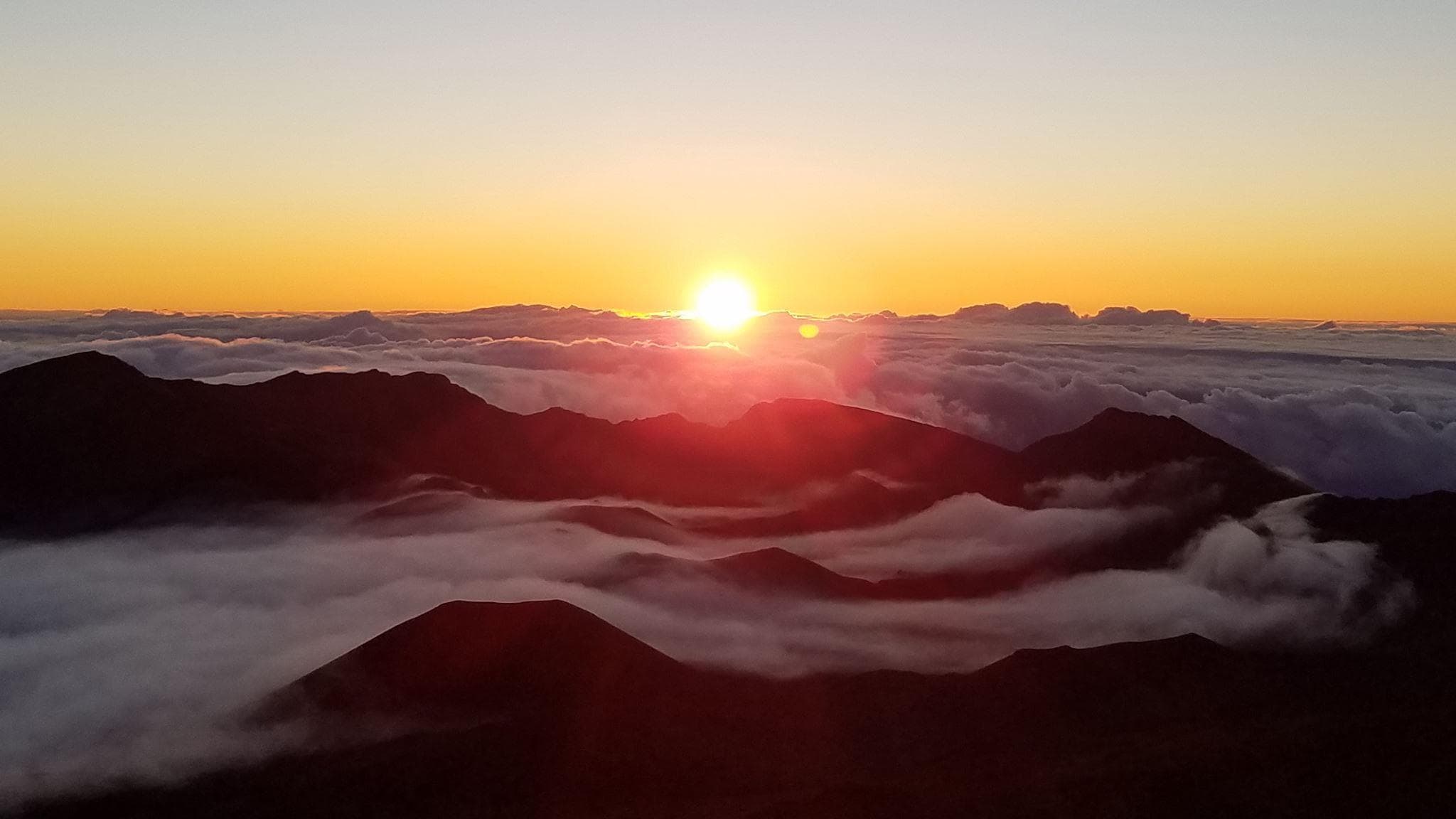 Cyclists watching sunrise above cloud inversion on Haleakala