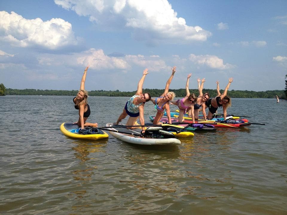 Group paddleboard class raising arms on river under clouds