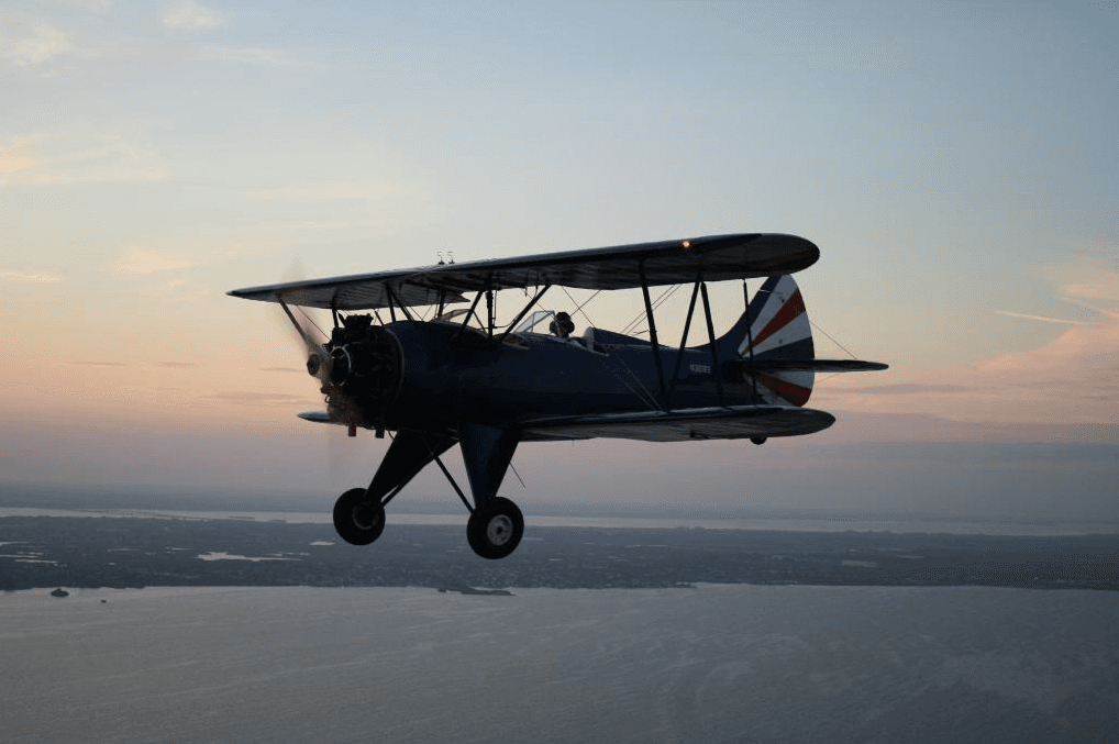 Vintage biplane silhouetted over coastal sunset flight
