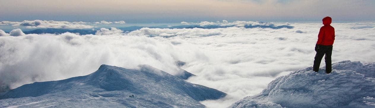 Hiker standing on snowy Mount Washington ridge above clouds