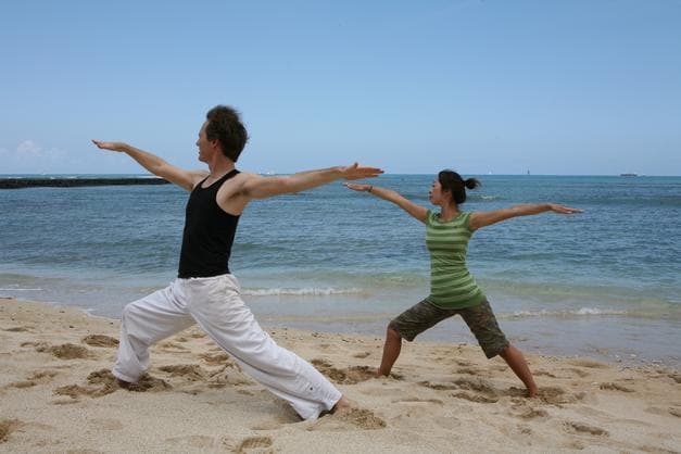 Two people practicing warrior yoga on sandy Waikiki beach