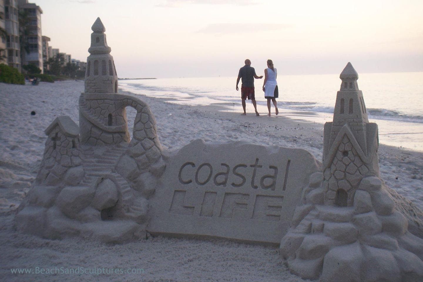Coastal sandcastle sculpture with walkers at sunset beach