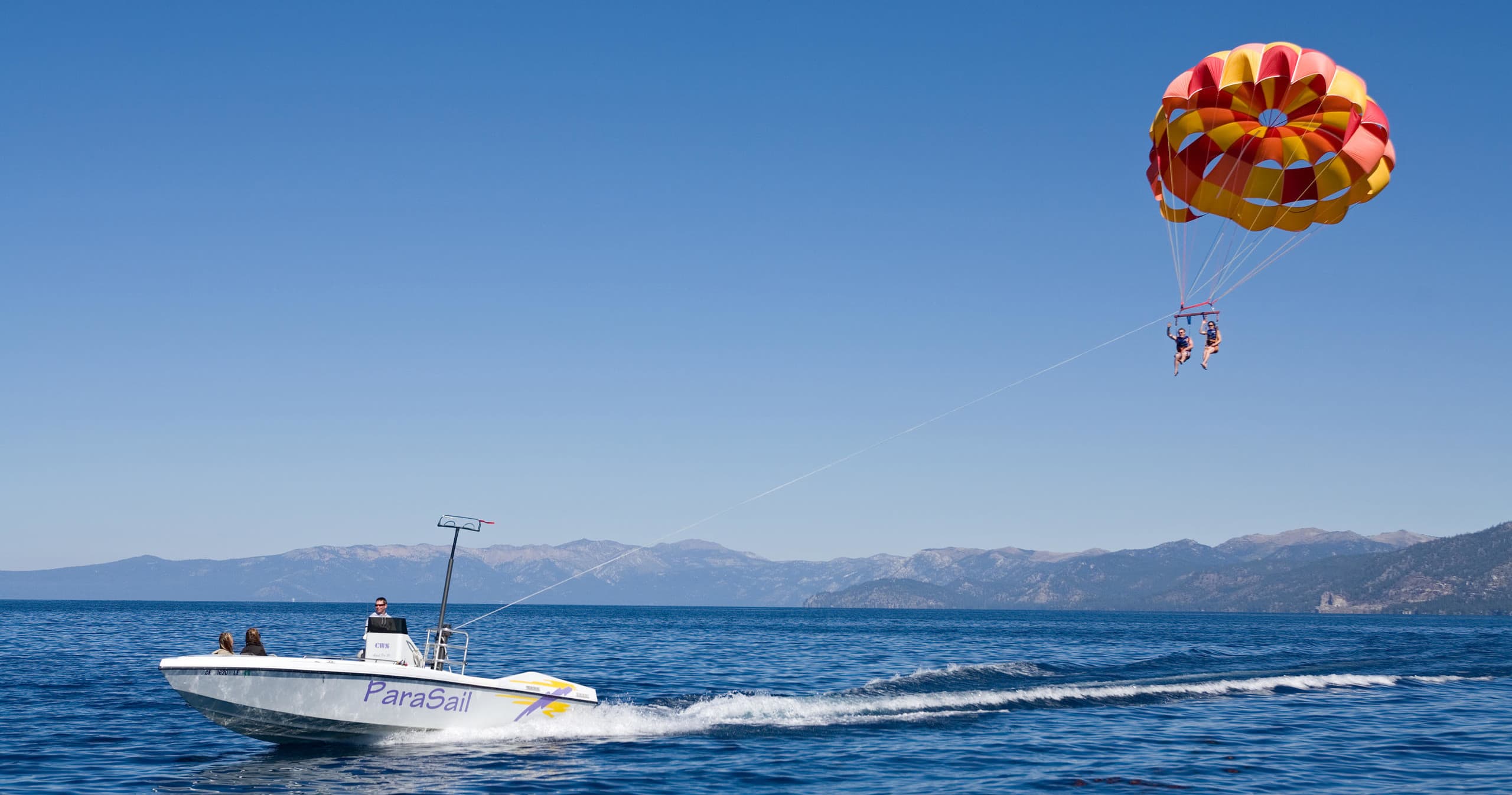 Boat with colorful parasail activity over clear lake waters at distance