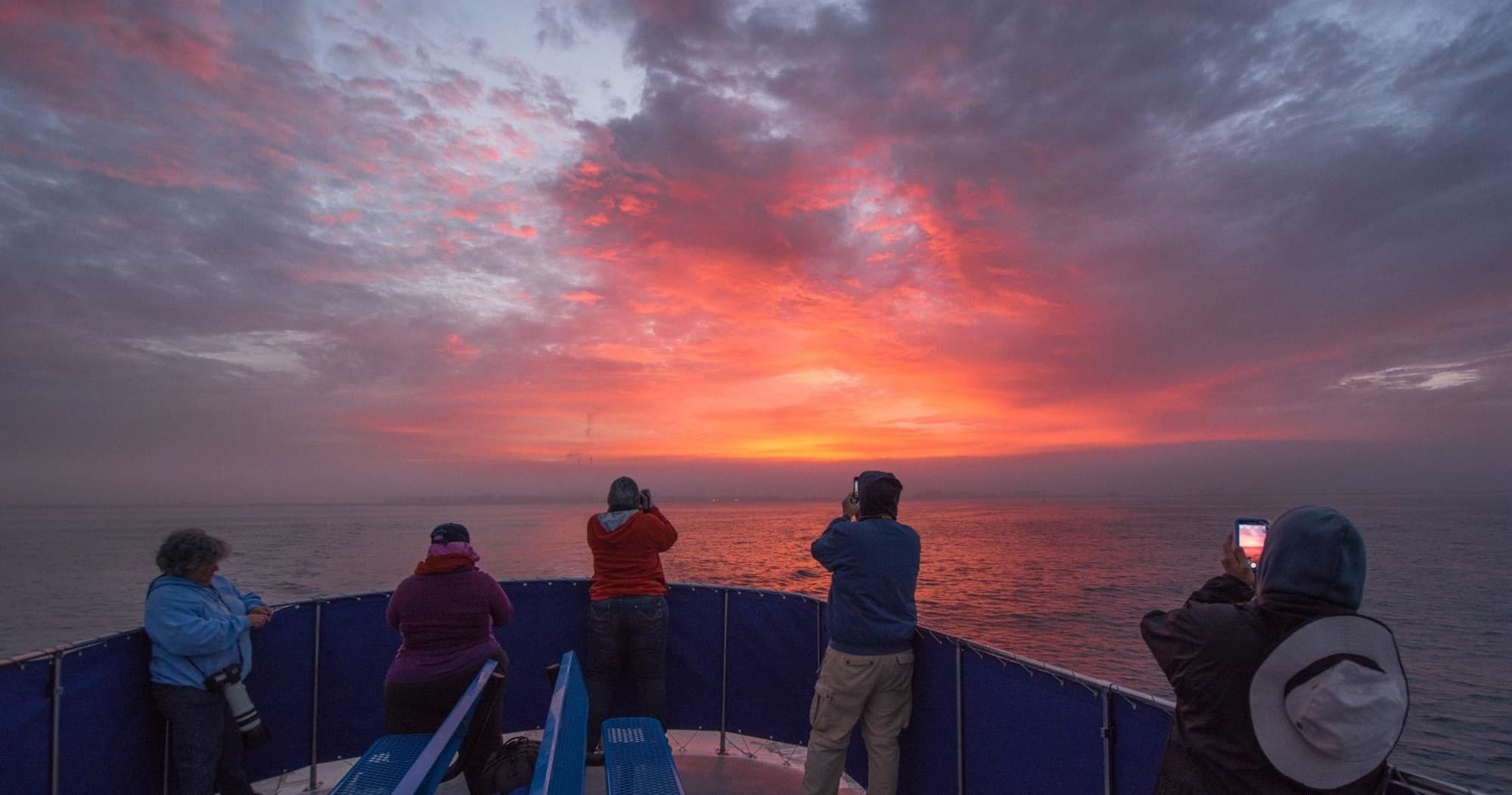 Passengers on sunset whale-watching tour photographing open ocean sky