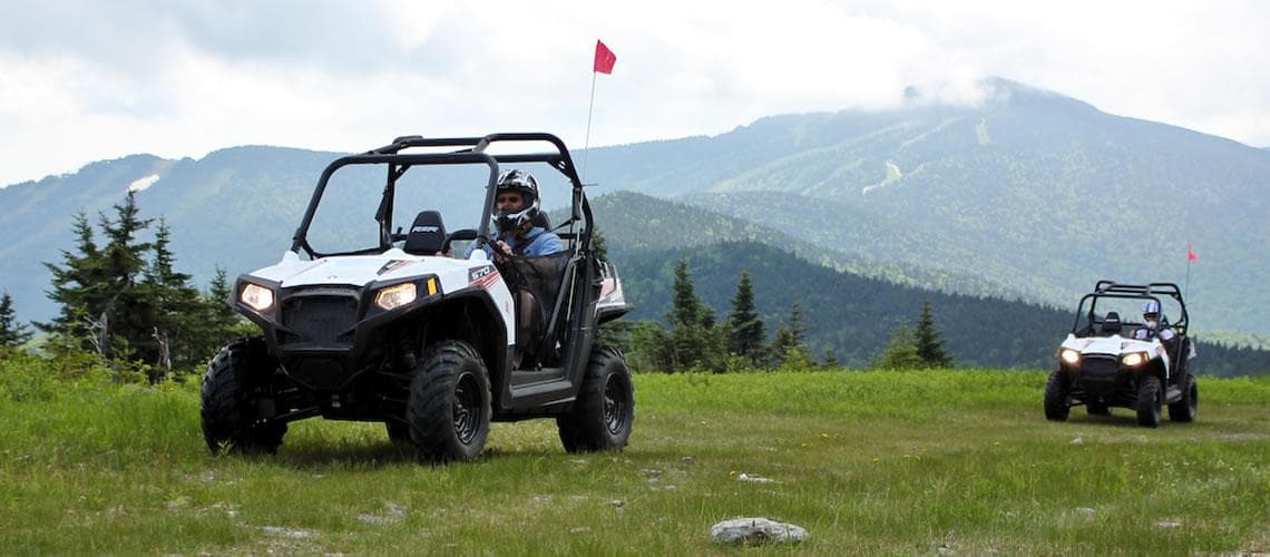 Two ATVs driving on grassy mountain ridge with scenic views