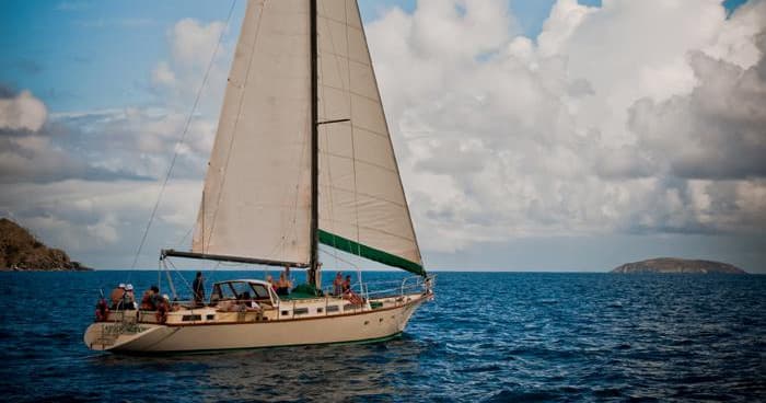 Classic sailboat cruising open sea under blue sky near islands