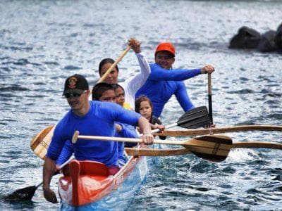 Outrigger canoe team paddling near rocky shoreline in ocean
