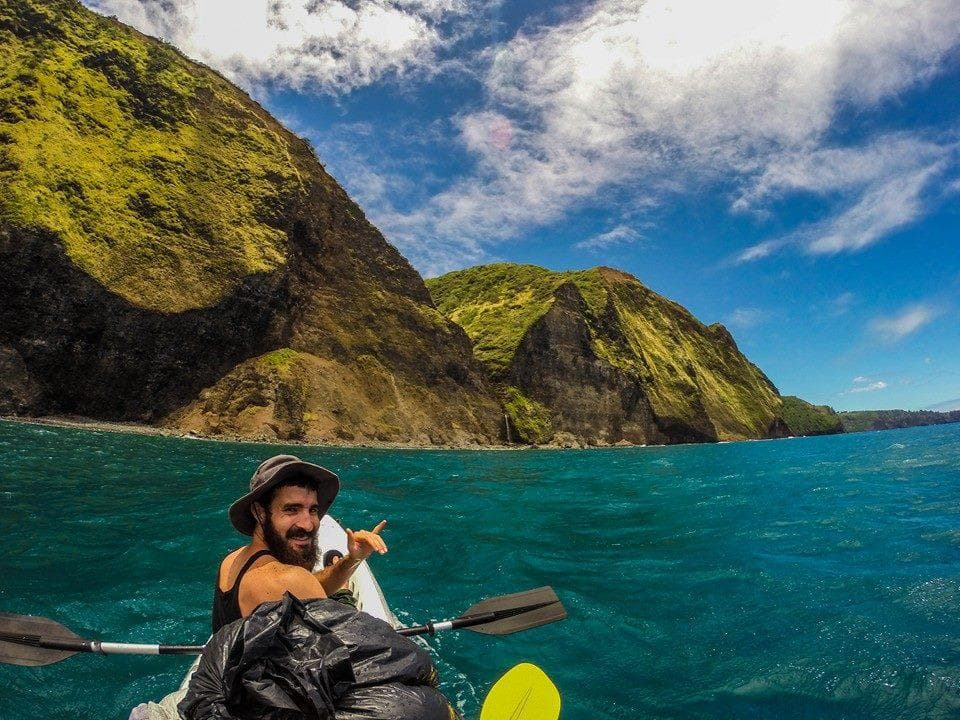 Solo kayaker paddling turquoise bay with volcanic cliffs