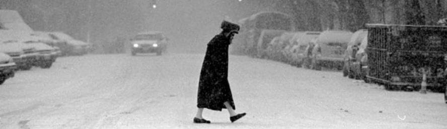 Person crossing snowy urban street on winter Hasidic neighborhood walk