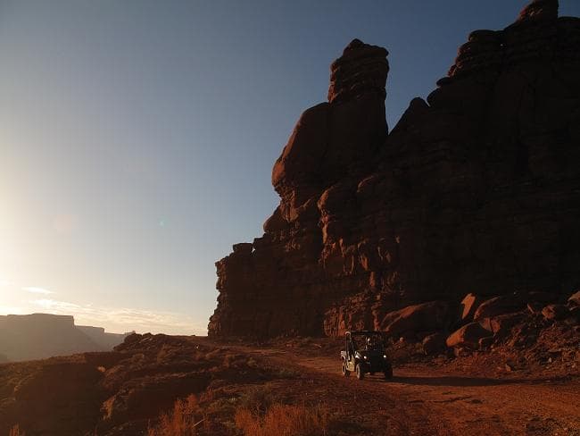 Red rock cliff silhouette at sunset with off-road vehicles on trail