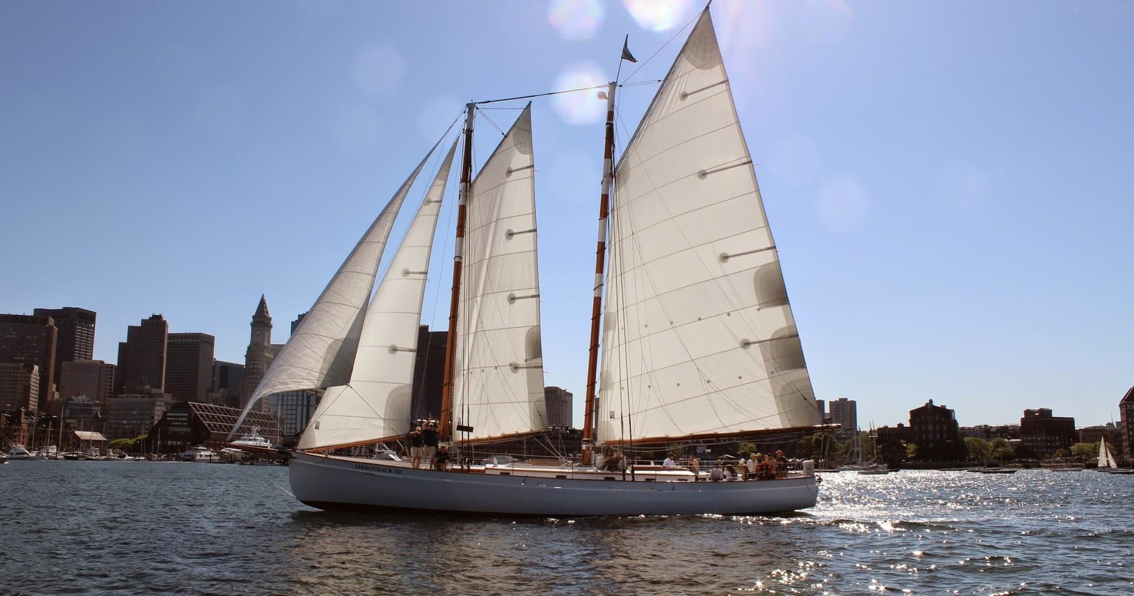 Tall sailboat cruising Boston Harbor with crew and city skyline