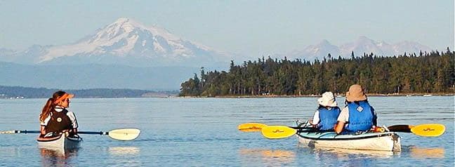 Sea kayakers paddling with snow-capped mountain backdrop