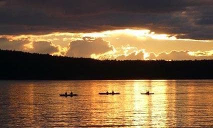 Kayaks silhouetted against dramatic sunset over open water