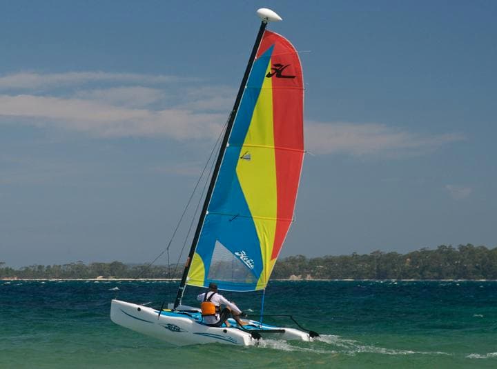 Small sailboat cruising open water with distant island shoreline