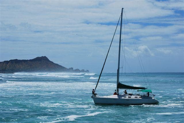 Sailboat cruising blue Pacific waters near rocky coastline