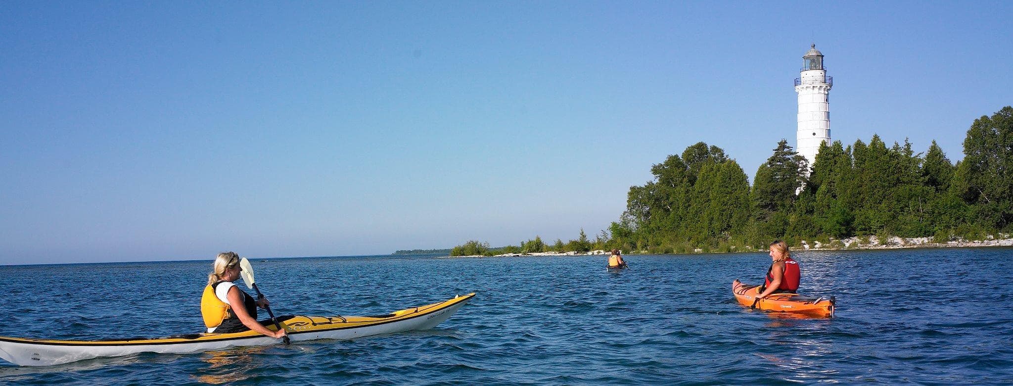 Kayakers paddling near lighthouse on Lake Michigan shoreline