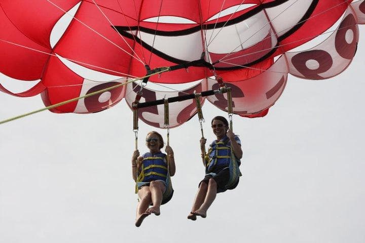 Two people tandem parasailing beneath colorful red canopy