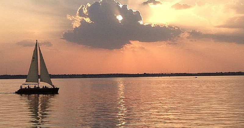 Sailboat silhouetted at golden sunset over calm bay waters