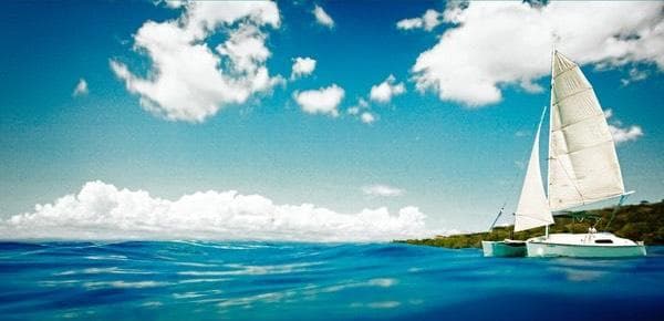 White sailboat cruising blue ocean under clouds, tropical coast