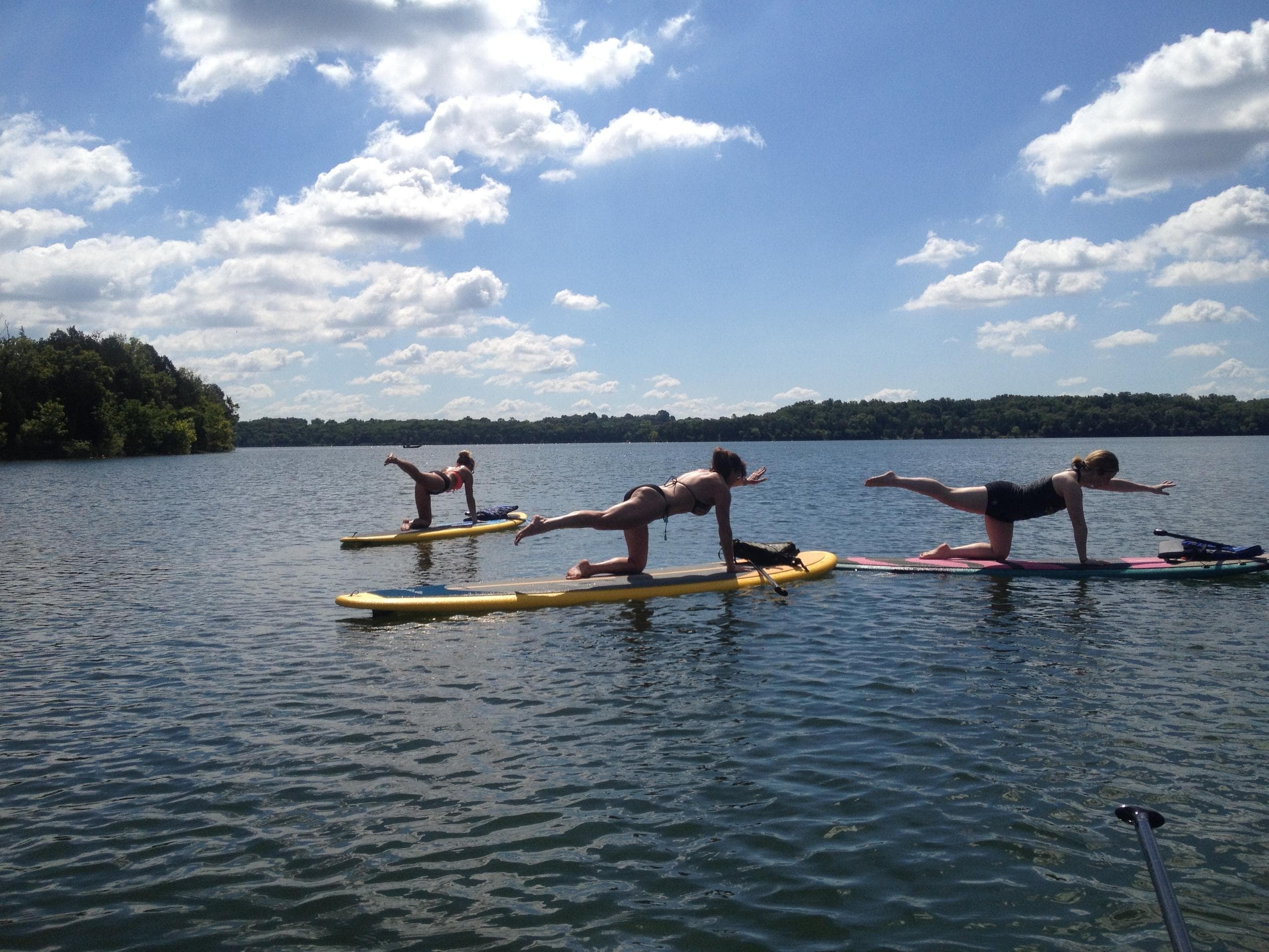 Stand-up paddleboard yoga on calm lake under blue sky