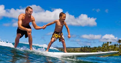 Instructor teaching young boy to surf on sunny reef break