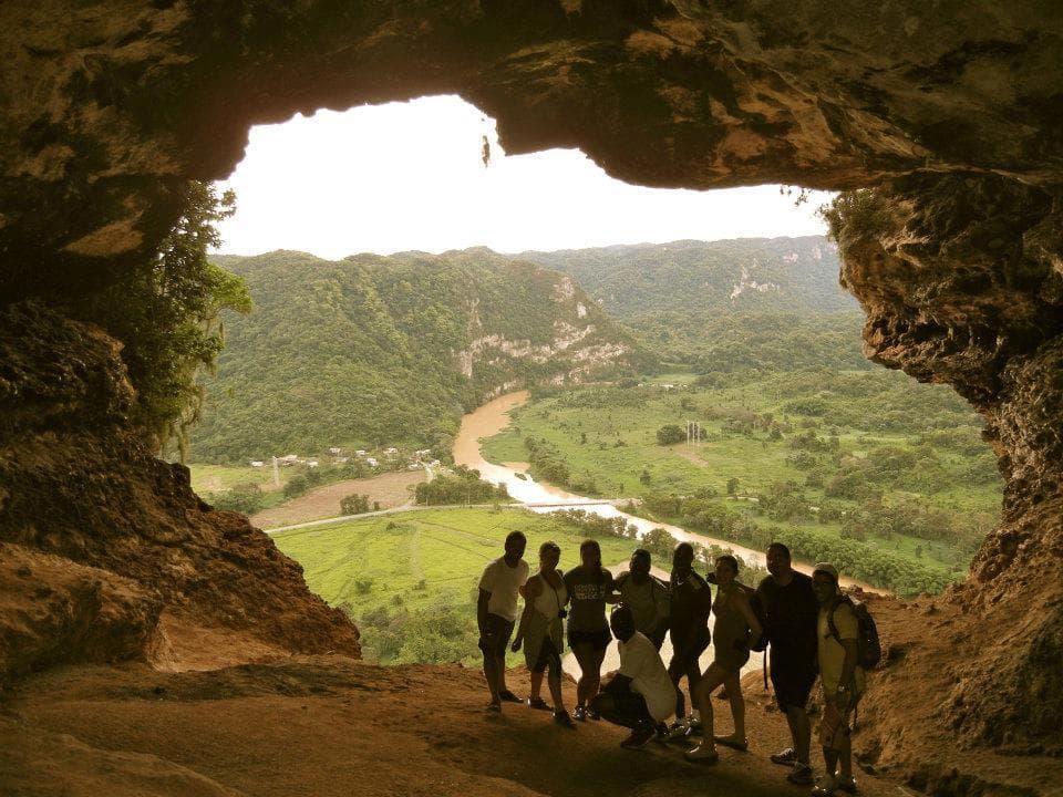 Hikers silhouetted in cave overlooking river valley vista in Cuba