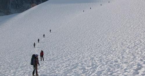 Climbers traversing steep snowy slope in glaciated alpine ascent