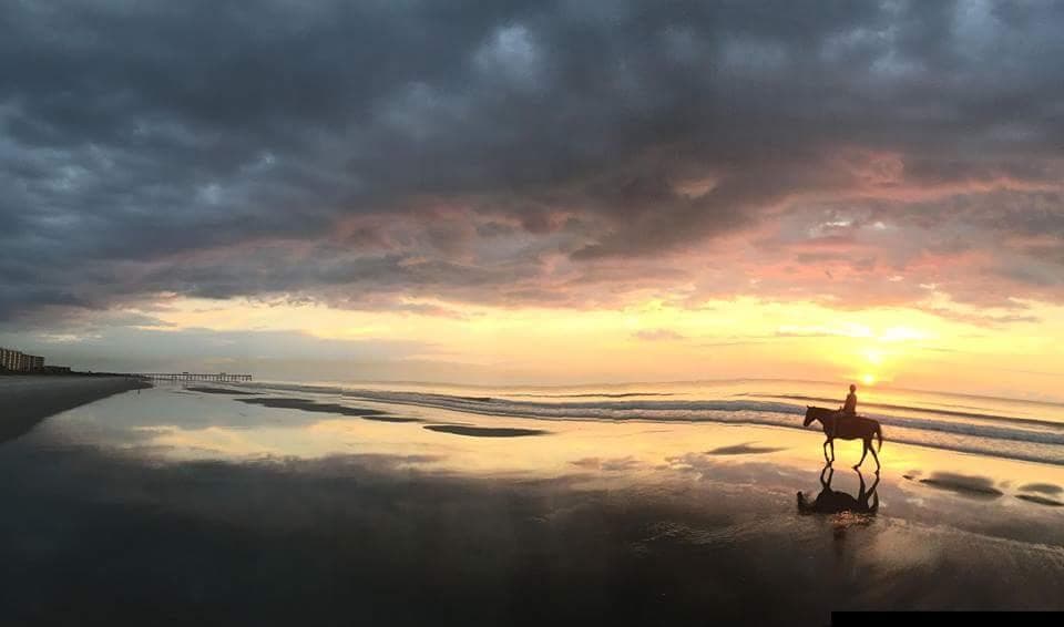 Sunset horseback ride with lone rider silhouetted on beach