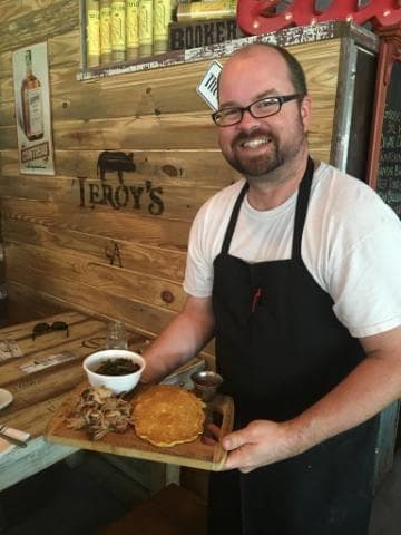 Local chef holding smoked meat platter inside rustic barbecue restaurant