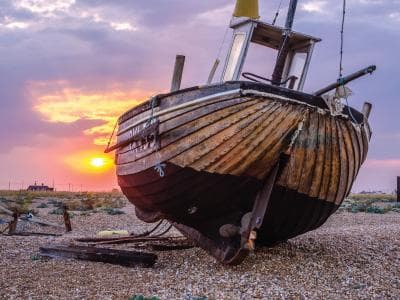 Abandoned wooden boat on pebbled beach at sunset shoreline