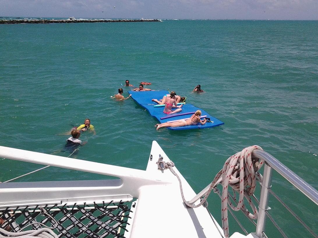 Guests lounging on floating mats in clear turquoise ocean near boat