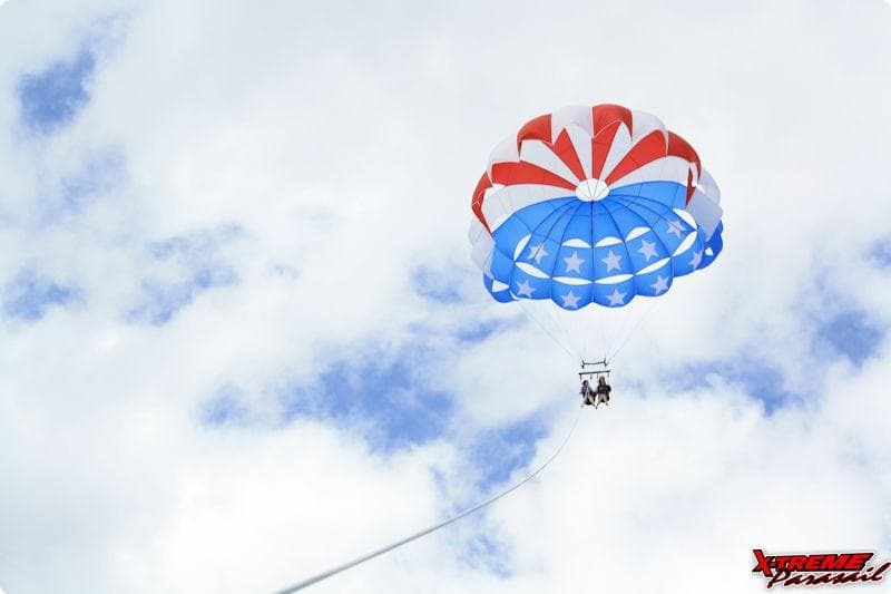 Tandem parasail high above bright cloudy sky over ocean