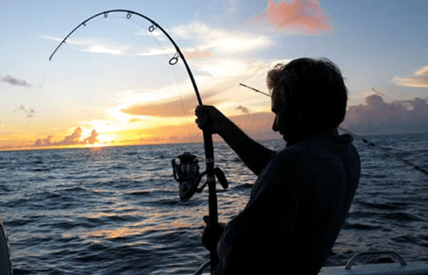 Angler fighting fish at sunset on offshore saltwater fishing trip