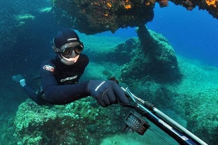 Spearfisher diving over rocky reef in clear ocean water