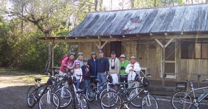 Guided bike tour group posing by rustic cabin on nature trail