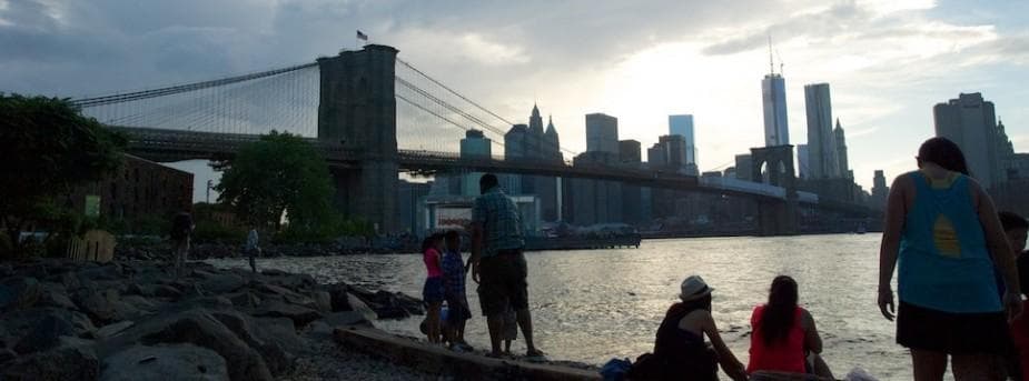 Brooklyn Bridge skyline at dusk with waterfront walkers