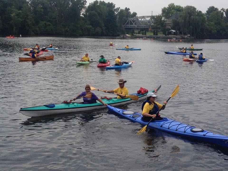 Multiple kayakers paddling across broad river or lake at sunset